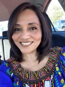 Smiling woman in colorful embroidered top.