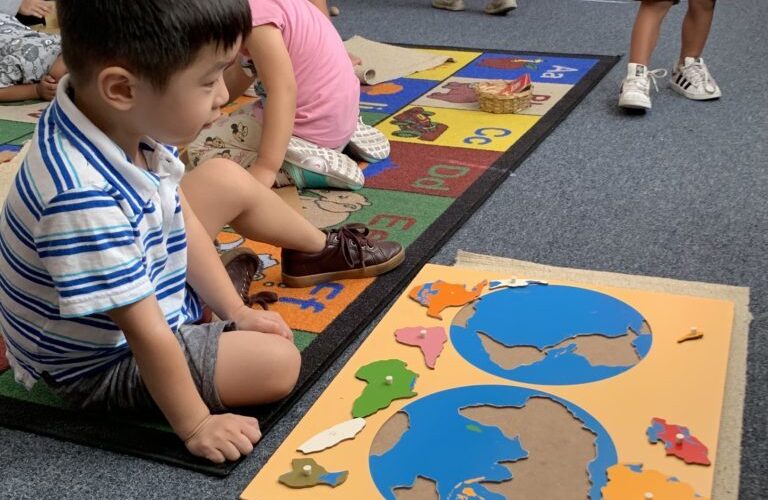 Child assembling world map puzzle on floor.